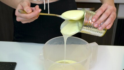 Hands pour condensed milk into a container for making cream.