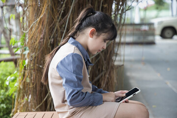 Smartphone and bad body posture concept, young Asian primary schoolgirl using smartphone with...