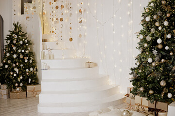A large Christmas tree in the living room, decorated with garlands and light balloons. Bright Christmas interior with a white staircase