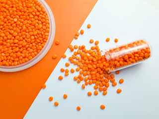 Orange masterbatch granules in glass tubes and cups on white and orange background.Color pigment...