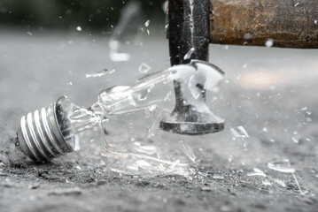 Closeup photo of hammer smashing old incandescent light bulb,Incandescent bulb being smashed by a hammer, glass fragments flying