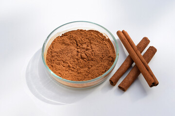 Cinnamon powder in a petri dish and cinnamon sticks, white background
