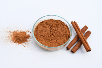 Cinnamon powder in a petri dish and cinnamon sticks, white background
