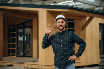 Cheerful facial expression. Male builder is at construction of wooden house