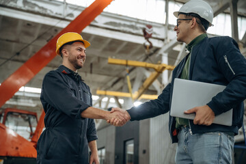Friendly handshake. Two male factory workers are in the warehouse
