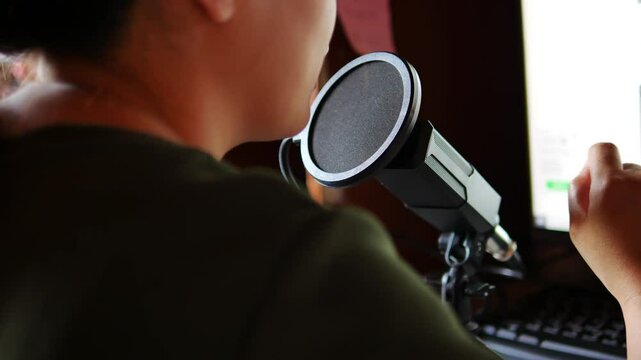  Asian woman using microphone recording podcast episode. Content creator speaking into microphone, engaging with audience in studio. Concept of podcasting, communication
