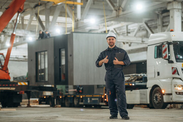 Part of the house is transported by a truck. Male worker is in the modern warehouse or manufacturing company