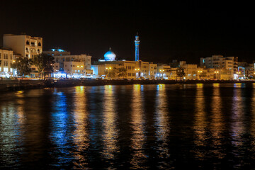 City of Muscat by night with lights reflecting on the water and the minaret illuminated in the skyline