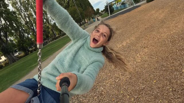 Selfie stick shot of happy young girl on playground cableway swing