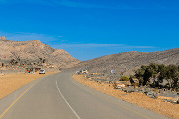 A winding road through the rugged landscape of Oman showcasing dramatic mountains and clear blue skies