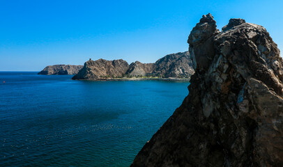 Obraz premium Majestic coastline of Oman with rugged cliffs and clear blue waters under bright sunny skies
