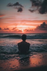 Fototapeta premium A lone figure in silhouette sits by ocean waves contemplating as the sun sets.