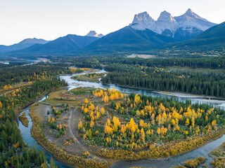 Aerial view of Canadian Rockies mountain range and Bow river forest at dawn in autumn. Canmore, Alberta, Canada. The Three Sisters trio of peaks.