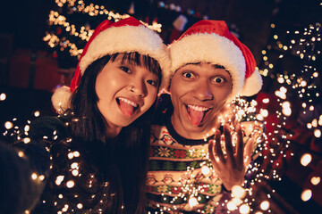 Portrait of two young people couple make selfie show tongue celebrate xmas new year garland lights...