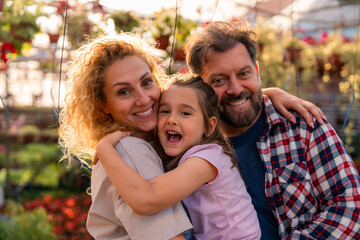 Heartwarming family moment as parents embrace their daughter, surrounded by the rich flora of their greenhouse.