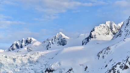Fototapeta premium Mountain peaks and snow in The Arctic, against a blue sky.