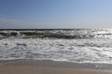 Sunny Beach with Waves Crashing on Shore Under Clear Blue Sky