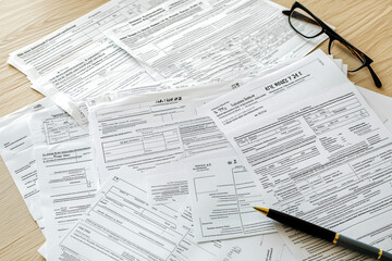 Tax Forms and Documents Scattered on Desk with Pen and Glasses