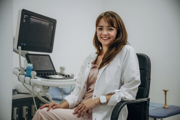 Sitting and smiling. Doctor is with ultrasound equipment is in the clinic in the room