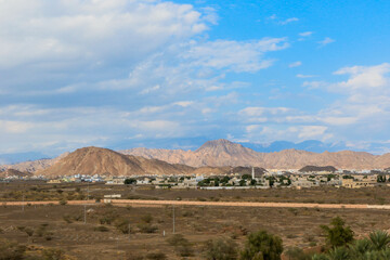 Vast desert landscape of Oman with mountains in the background under a dramatic sky during the day