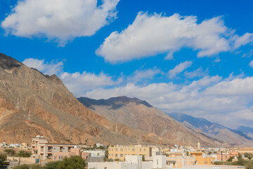 Obraz premium A breathtaking view of the mountains and sky over a typical Oman town during a sunny day with scattered clouds