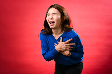 An Asian woman in a blue sweater clutches her chest in apparent distress, as if experiencing sudden...