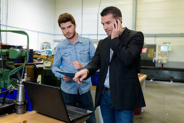 manager on cellphone pointing at laptop on the side