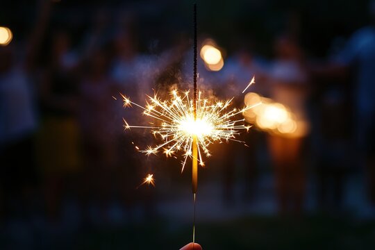 Hand holding lit sparkler at dusk, party vibe