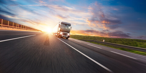 European truck driving on the asphalt road in rural landscape at sunset