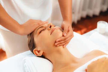 Caucasian woman enjoying relaxing anti-stress head massage and pampering facial beauty skin recreation leisure in dayspa modern light ambient at luxury resort or hotel spa salon. Quiescent