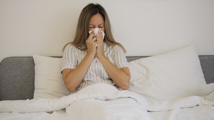 A sick woman with cold coughs into tissue, showing her struggle with disease. A close-up of disease affecting her as she coughs repeatedly into tissue. The frame clearly depicts illness and discomfort