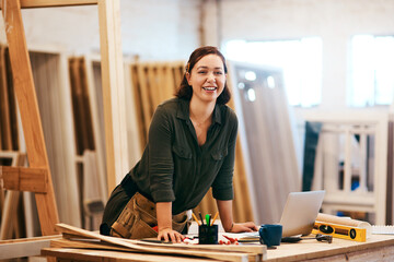 Laptop, portrait and smile of carpenter woman in workshop for professional joinery or woodworking. Computer, craftsmanship and creative with happy artisan or engineer in industry warehouse for design