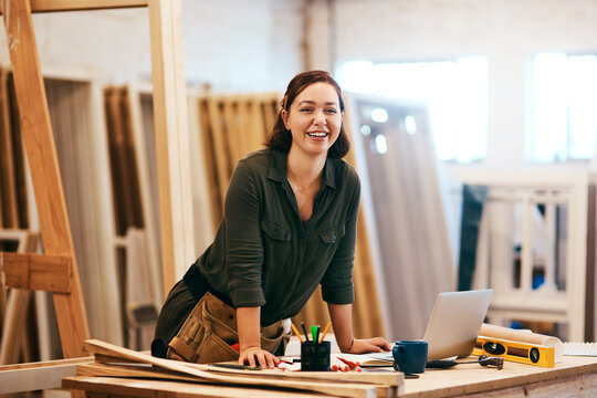Laptop, portrait and smile of carpenter woman in workshop for professional joinery or woodworking. Computer, craftsmanship and creative with happy artisan or engineer in industry warehouse for design