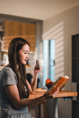 Reading book while enjoying cup of coffee, young woman sits at wooden table in cozy kitchen. warm light creates serene atmosphere, perfect for relaxation and reflection