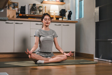 woman practices meditation in cozy indoor space, sitting cross legged on yoga mat. She exudes calmness and tranquility, surrounded by minimalist kitchen setting