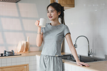 young woman in gray outfit enjoys cup of coffee in modern kitchen, radiating relaxed and cheerful...
