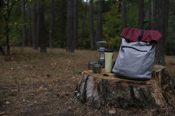 tourism. tourist gray and burgundy backpack, metal mugs and thermos, lantern with compass in the forest