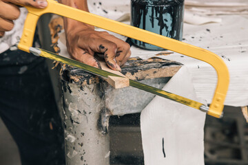 Hands of an unrecognizable person cutting a strip of wood with a saw