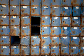 Large amount of rusted blue mail boxes at an abandoned post office.  Some of the boxes are missing their doors.  