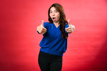 An asian cheerful woman wearing a blue sweater and black pants smiles while giving two enthusiastic...
