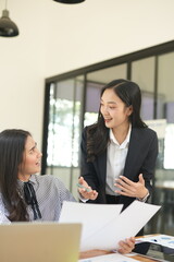  Two professional business executives working on laptop computer sitting at office desk, happy colleagues discussing company digital strategy.