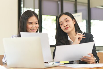 Group of happy Asian business people having a meeting at the office. Two women working together using modern laptops.