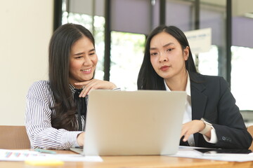 Group of happy Asian business people having a meeting at the office. Two women working together using modern laptops.