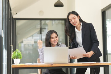 Group of happy Asian business people having a meeting at the office. Two women working together using modern laptops.