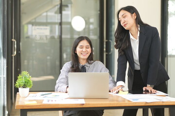  Group of happy Asian business people having a meeting at the office. Two women working together using modern laptops.