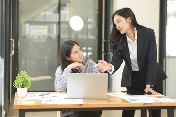 Fototapeta premium Group of happy Asian business people having a meeting at the office. Two women working together using modern laptops.