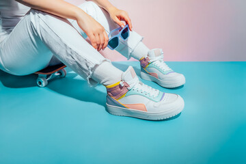 Close up female legs in white jeans and retro style high-top multicolor sport sneakers shoes...
