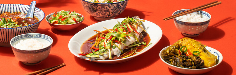 Chinese Lunar New Year festive table. Cantonese-Style recipes  Sea bass or Spigola fish steamed with ginger, red peppers in soy sauce with Chinese cabbage, traditional spicy soup and rice, banner