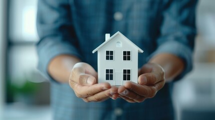 Hands holding a small white house model, symbolizing real estate, home ownership, and investment. Focus on future and possibilities.