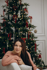 Obraz premium cute girl sitting near christmas tree, new year eve